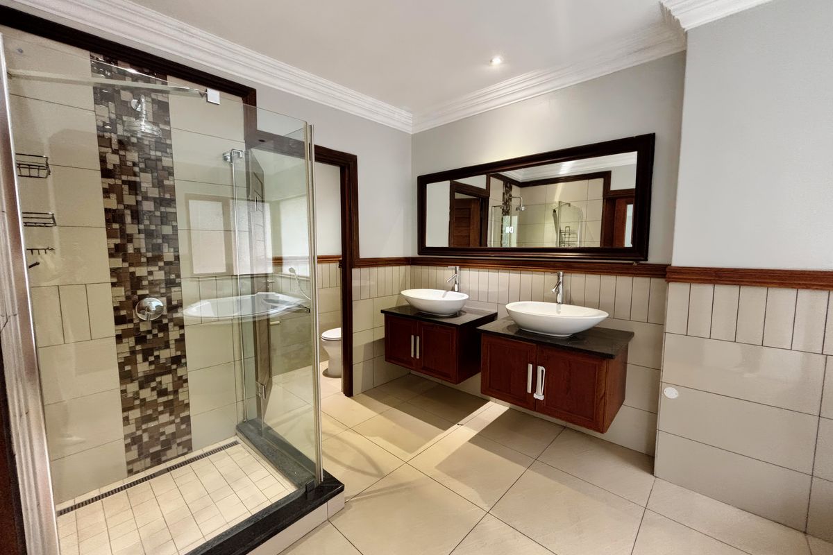 A well-maintained bathroom featuring a double vanity with vessel sinks, a glass-enclosed shower with mosaic accents, and neutral floor tiling.