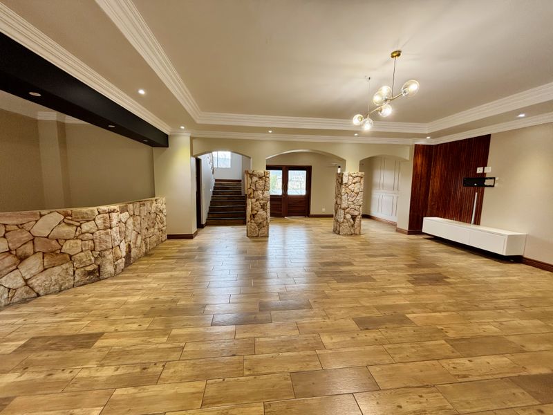 Spacious open-plan living area featuring stone-clad pillars, wood-look tile flooring, crown molding, and elegant timber wall paneling.