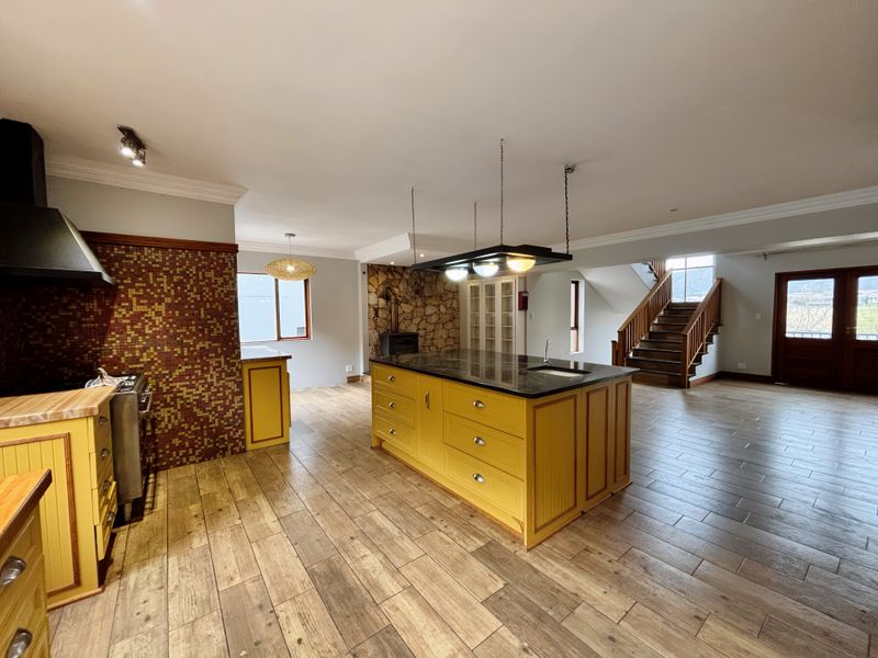 Spacious open-plan kitchen featuring a central island with granite countertop, stone feature wall with fireplace, and timber staircase leading to the upper level.