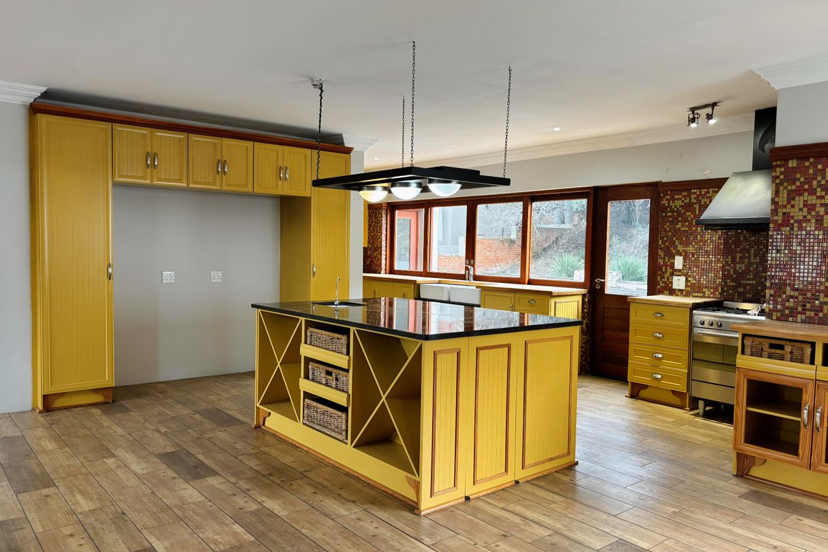 Spacious kitchen featuring yellow cabinetry, a large central island with granite countertop, mosaic tile backsplash, and wood-look tile flooring.