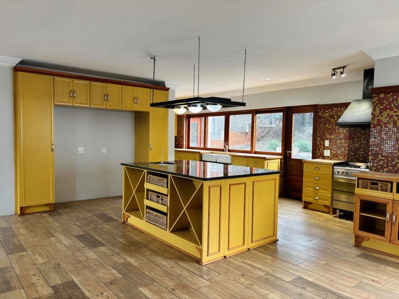Spacious kitchen featuring yellow cabinetry, a large central island with granite countertop, mosaic tile backsplash, and wood-look tile flooring.