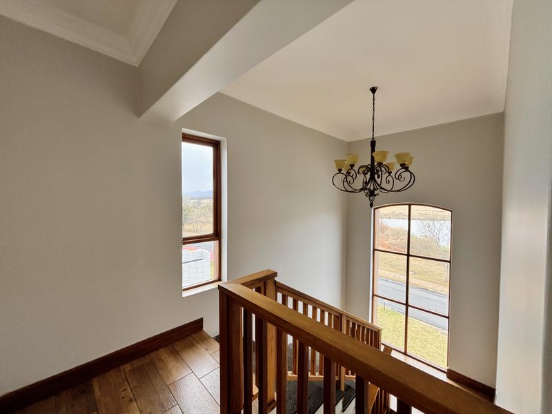 A bright, spacious landing area featuring a wooden staircase with a matching balustrade, elegant chandelier, and large windows offering scenic views.