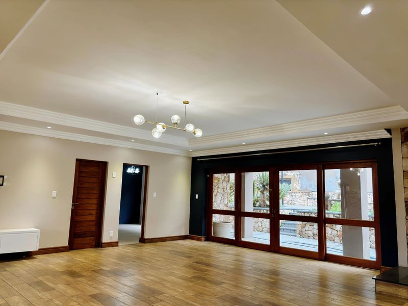 Spacious living room featuring wooden flooring, recessed ceiling with crown molding, modern chandelier, and large sliding doors providing access to the outdoor area.