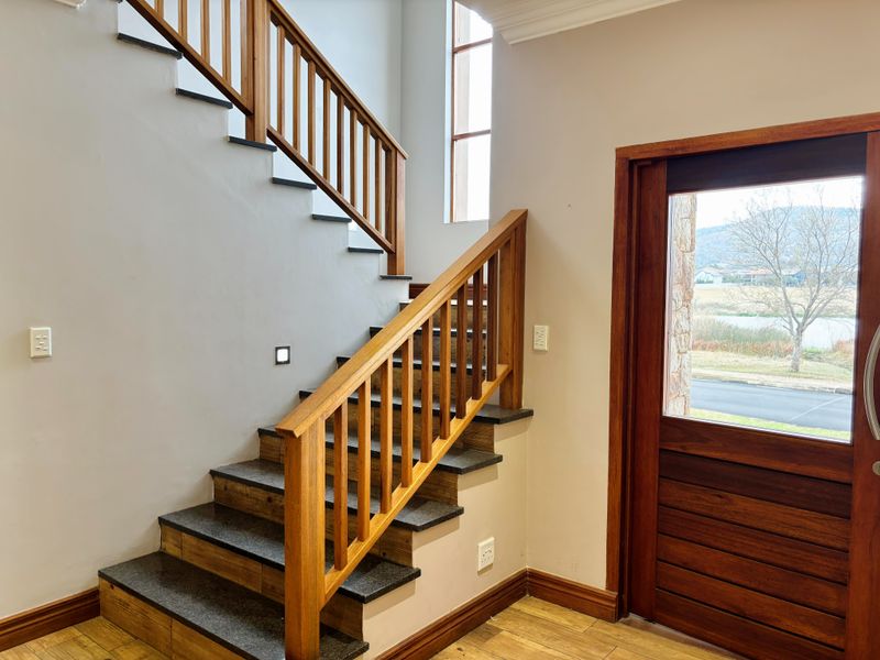 Bright entrance foyer featuring a modern wooden staircase with stone treads, a solid timber front door, and clean neutral wall finishes.