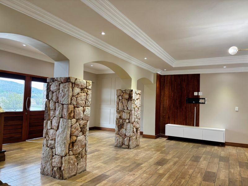 Spacious living area featuring distinctive stone-clad columns, timber wall paneling, crown molding, and high-quality timber-look floor tiles in a well-maintained interior space.