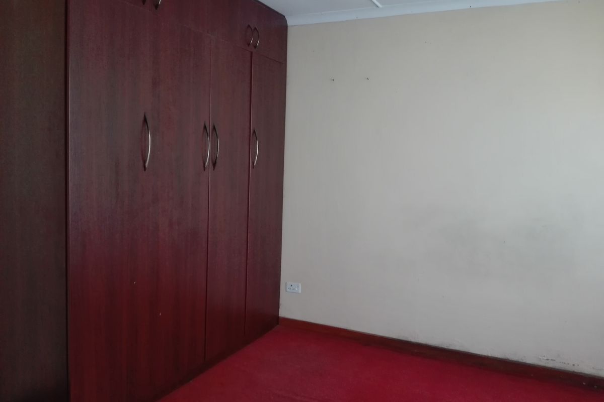 A vacant bedroom featuring dark wood built-in cupboards, red carpeting, and neutral walls, offering a blank canvas for potential updates.