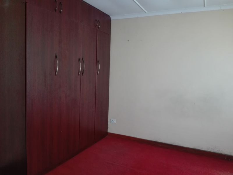 A vacant bedroom featuring dark wood built-in cupboards, red carpeting, and neutral walls, offering a blank canvas for potential updates.