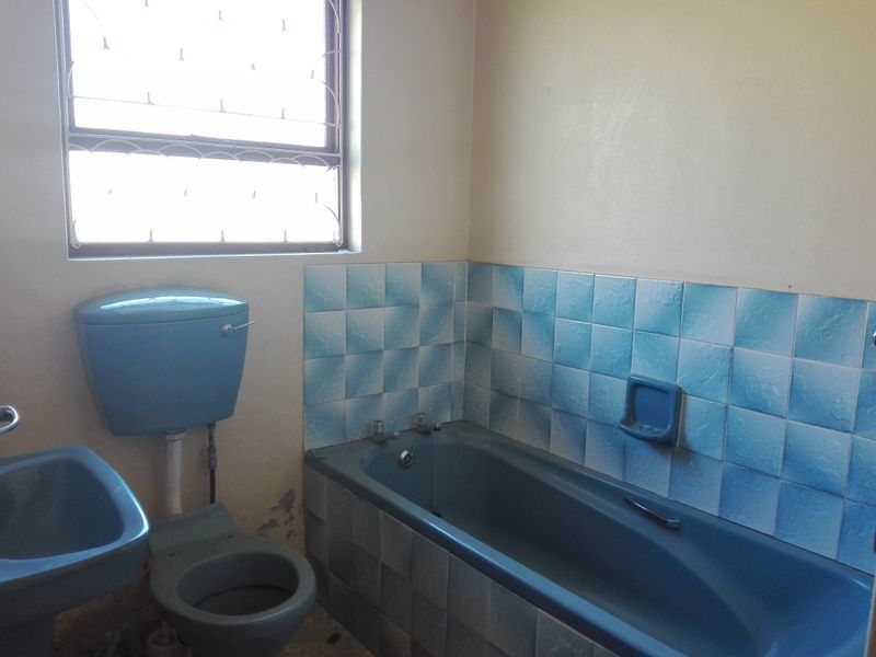 A dated bathroom featuring a blue bathtub, matching toilet, and pedestal basin with blue tiled splashbacks and security bars on the window.