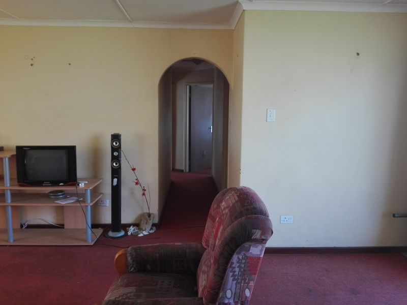 A living room area featuring an arched doorway leading to a hallway, with carpeted flooring and plain wall finishes.