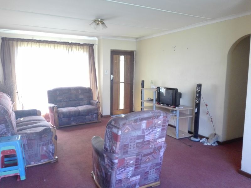 A dated living room featuring a timber entrance door, an arched entryway, and carpeted flooring, offering potential for modernization and cosmetic updates.