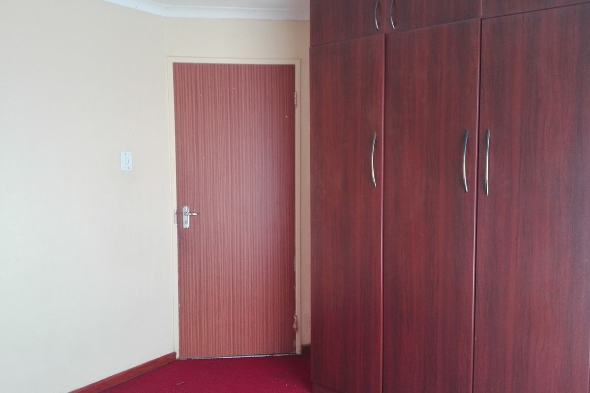 A bedroom featuring built-in wooden cupboards, red carpeting, and a standard interior door.