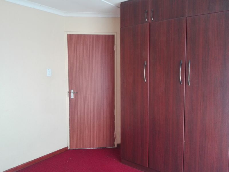 A bedroom featuring built-in wooden cupboards, red carpeting, and a standard interior door.