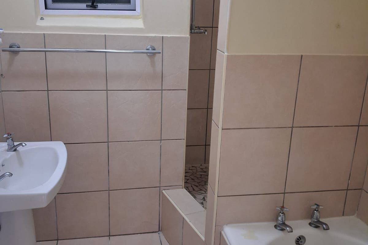 A functional bathroom featuring a pedestal basin, built-in bathtub, and a separate shower enclosure with neutral wall and floor tiling.