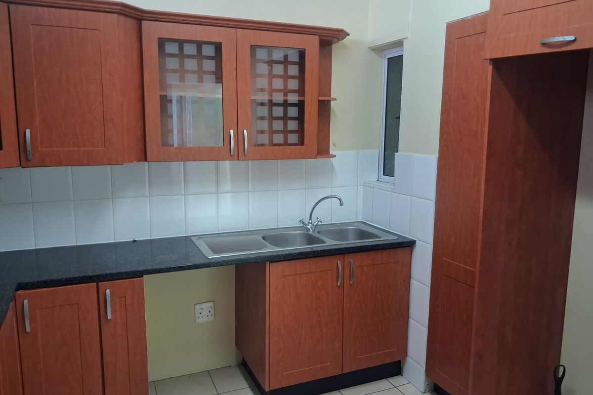 A functional kitchen featuring wooden cabinetry, granite countertops, a double sink, and tiled finishes, offering a clean and practical workspace.