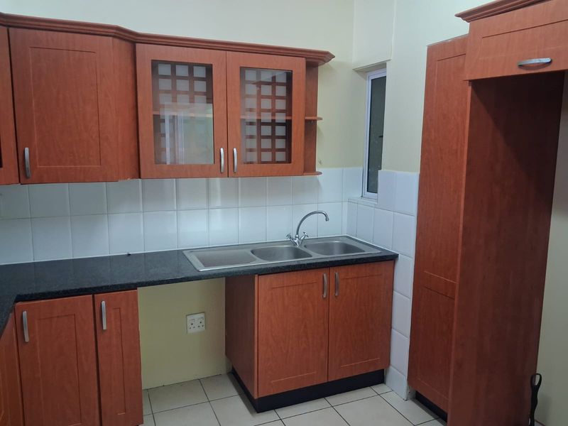 A functional kitchen featuring wooden cabinetry, granite countertops, a double sink, and tiled finishes, offering a clean and practical workspace.