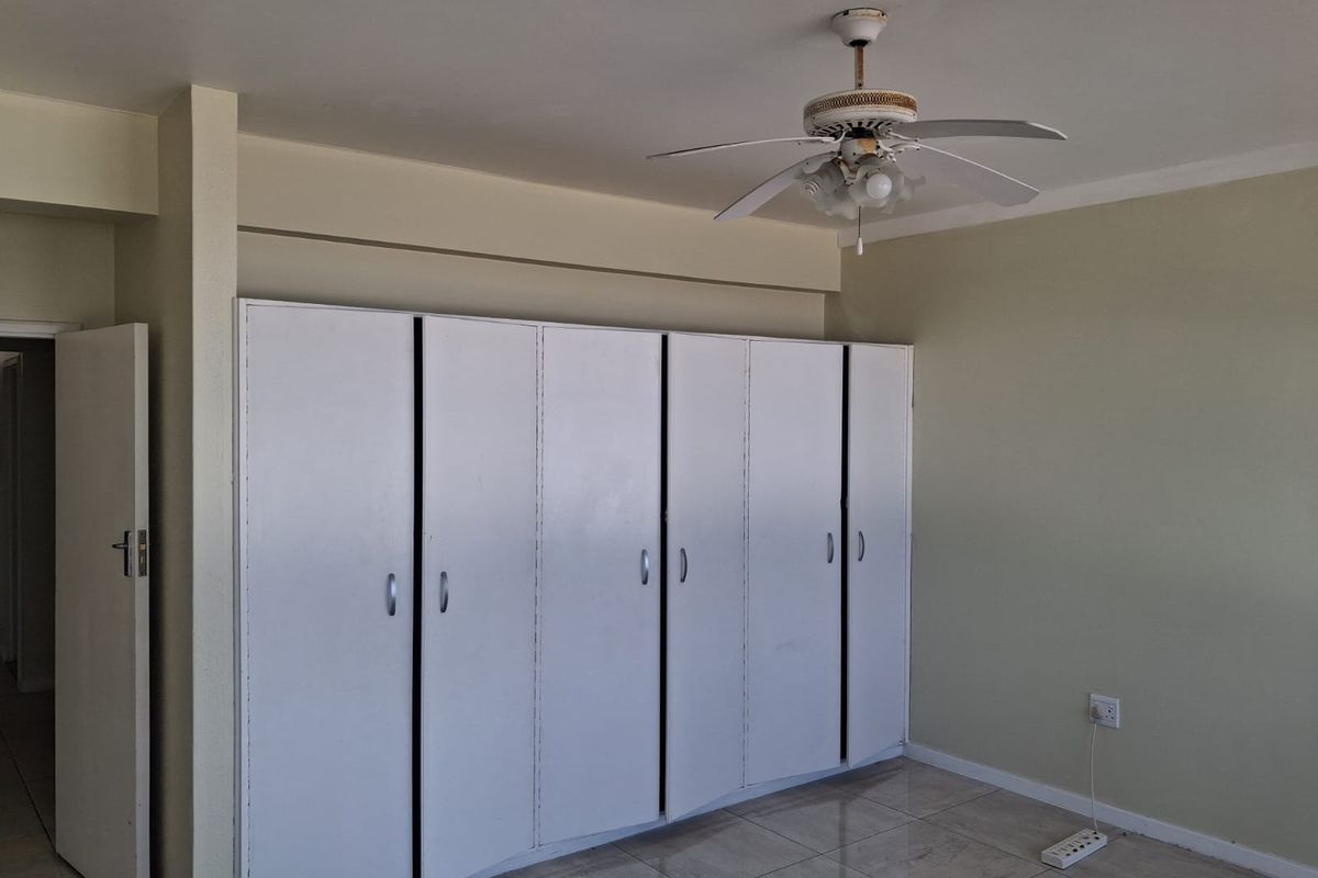 A spacious bedroom featuring neutral walls, tiled flooring, a ceiling fan, and extensive built-in cupboard storage.