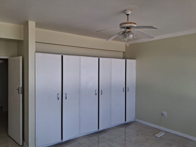 A spacious bedroom featuring neutral walls, tiled flooring, a ceiling fan, and extensive built-in cupboard storage.