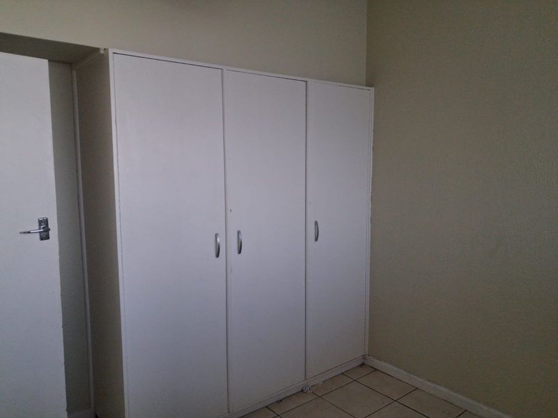 A simple bedroom featuring neutral walls, tiled flooring, and a functional built-in wardrobe.