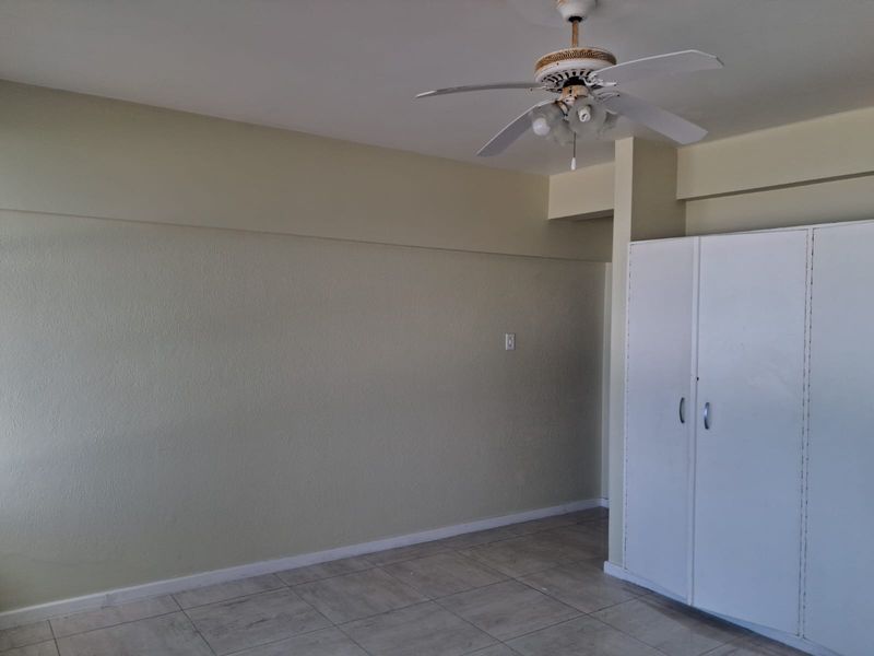 A clean, empty bedroom featuring neutral wall tones, tiled flooring, a ceiling fan, and a built-in wardrobe for storage.