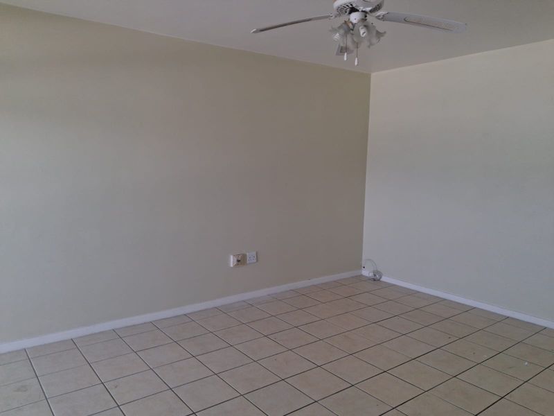 An empty living room featuring neutral wall paint, ceramic floor tiles, and a ceiling fan, providing a blank canvas for interior design.