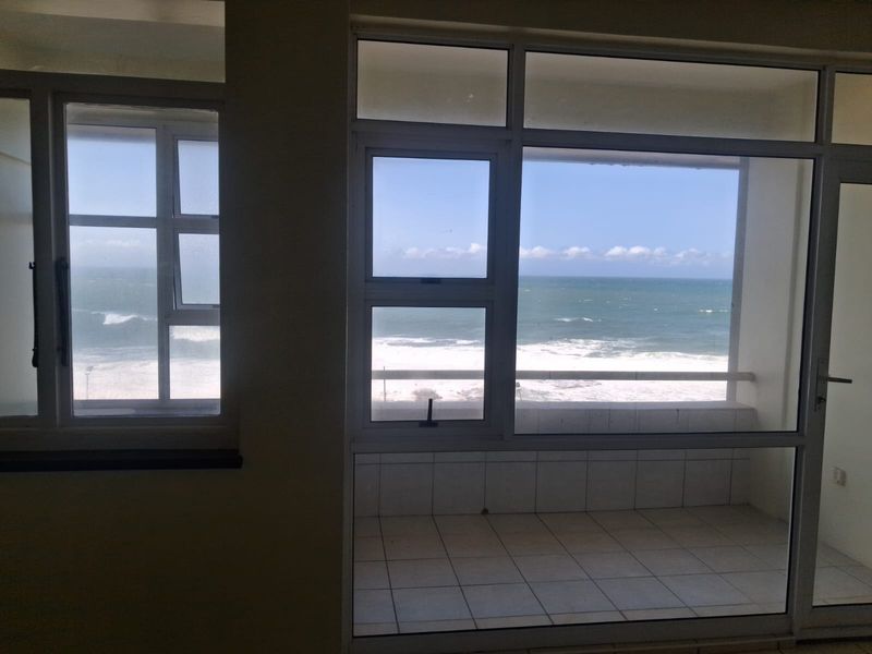 An enclosed balcony featuring tiled flooring and expansive windows offering direct ocean views, providing a bright and airy space.