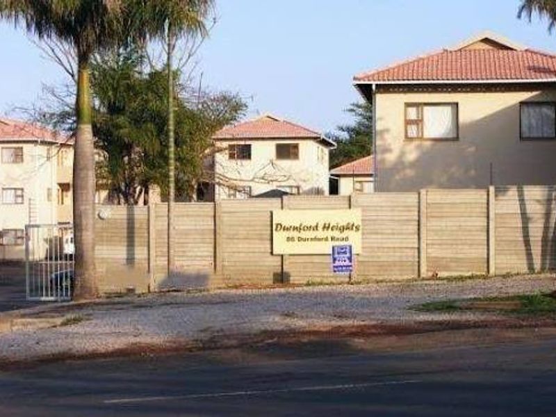 Street view of the Durnford Heights townhouse complex, featuring a secure gated entrance, precast boundary walling, and multi-story residential units with tiled roofs.