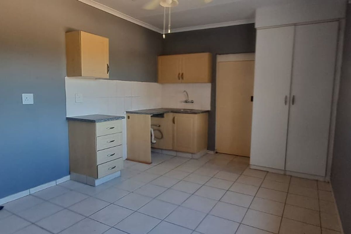 A compact kitchen area featuring tiled flooring, built-in cabinetry, and a sink, currently in need of cosmetic updates and repairs.