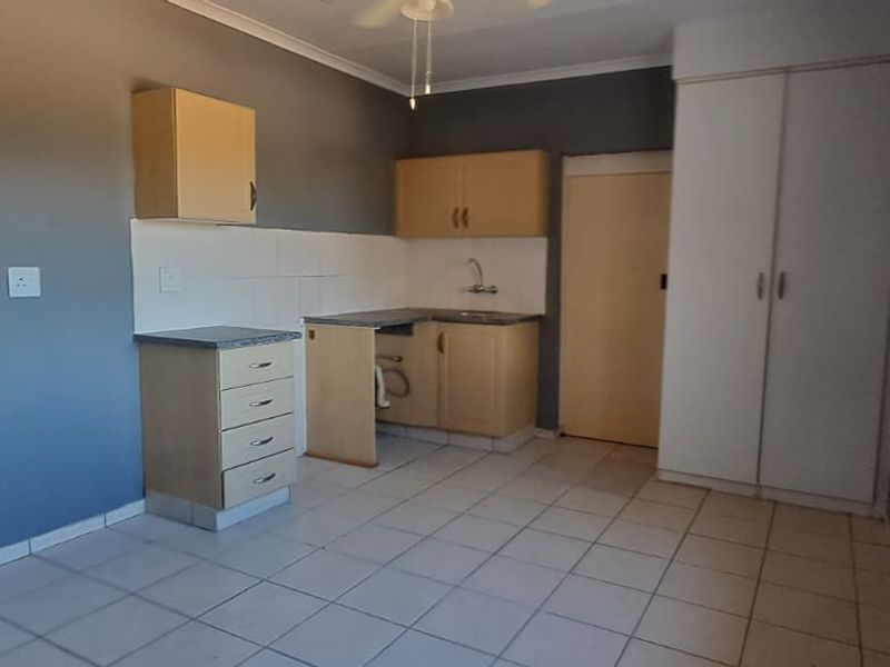 A compact kitchen area featuring tiled flooring, built-in cabinetry, and a sink, currently in need of cosmetic updates and repairs.