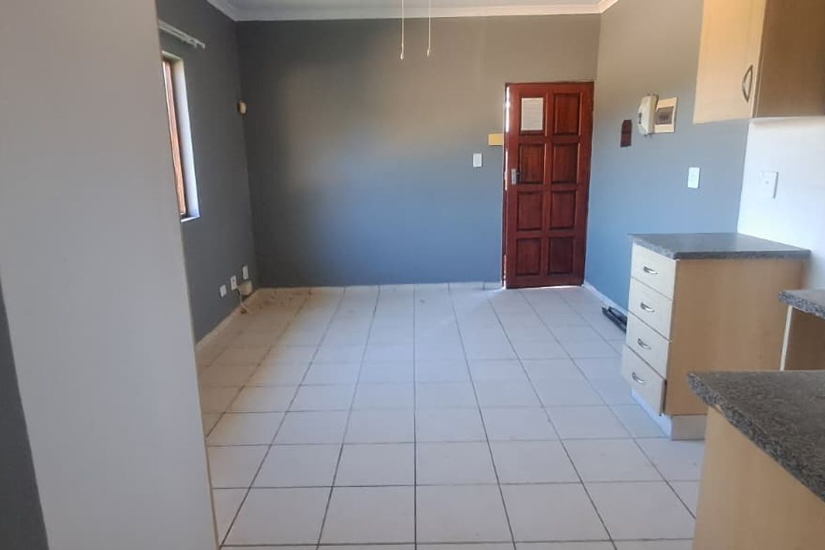 An open-plan living and kitchen area featuring tiled flooring, built-in cabinetry with laminate countertops, and direct access to the entrance.