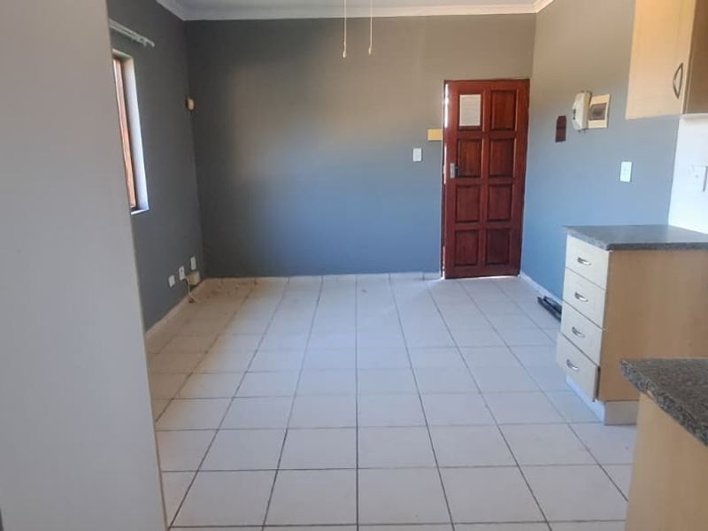 An open-plan living and kitchen area featuring tiled flooring, built-in cabinetry with laminate countertops, and direct access to the entrance.