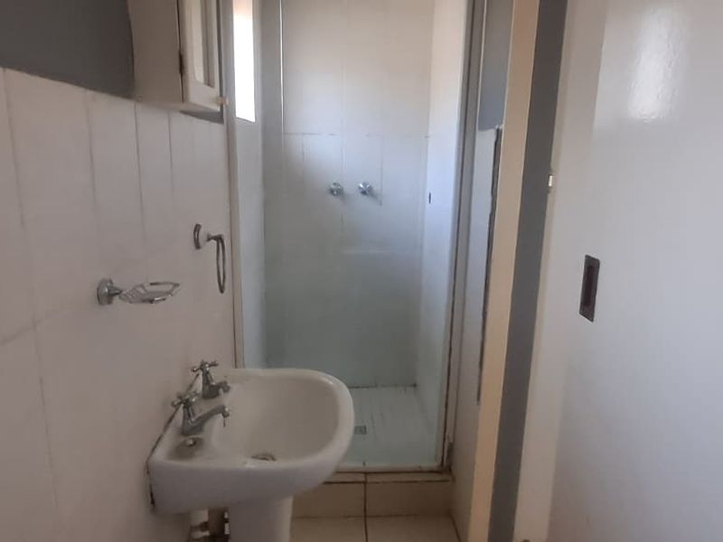 A functional bathroom featuring a pedestal basin and a separate shower enclosure with tiled walls and flooring.