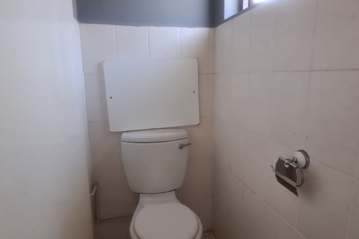 A compact bathroom featuring a standard toilet and tiled walls, currently in need of cosmetic updates and maintenance.