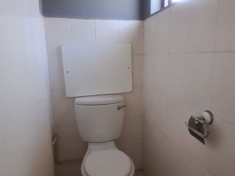 A compact bathroom featuring a standard toilet and tiled walls, currently in need of cosmetic updates and maintenance.