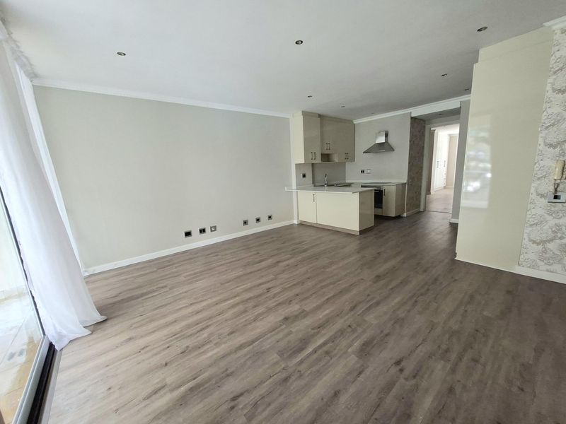 Spacious open-plan living area featuring modern laminate flooring, recessed lighting, and a compact, functional kitchen with built-in cabinetry and appliances.