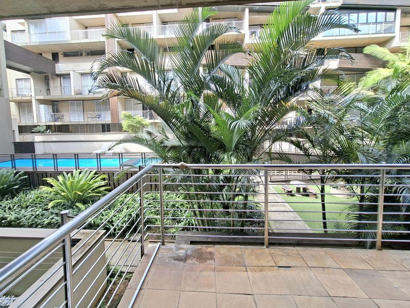 A spacious balcony with stainless steel railings overlooking the complex's communal swimming pool and landscaped garden area.