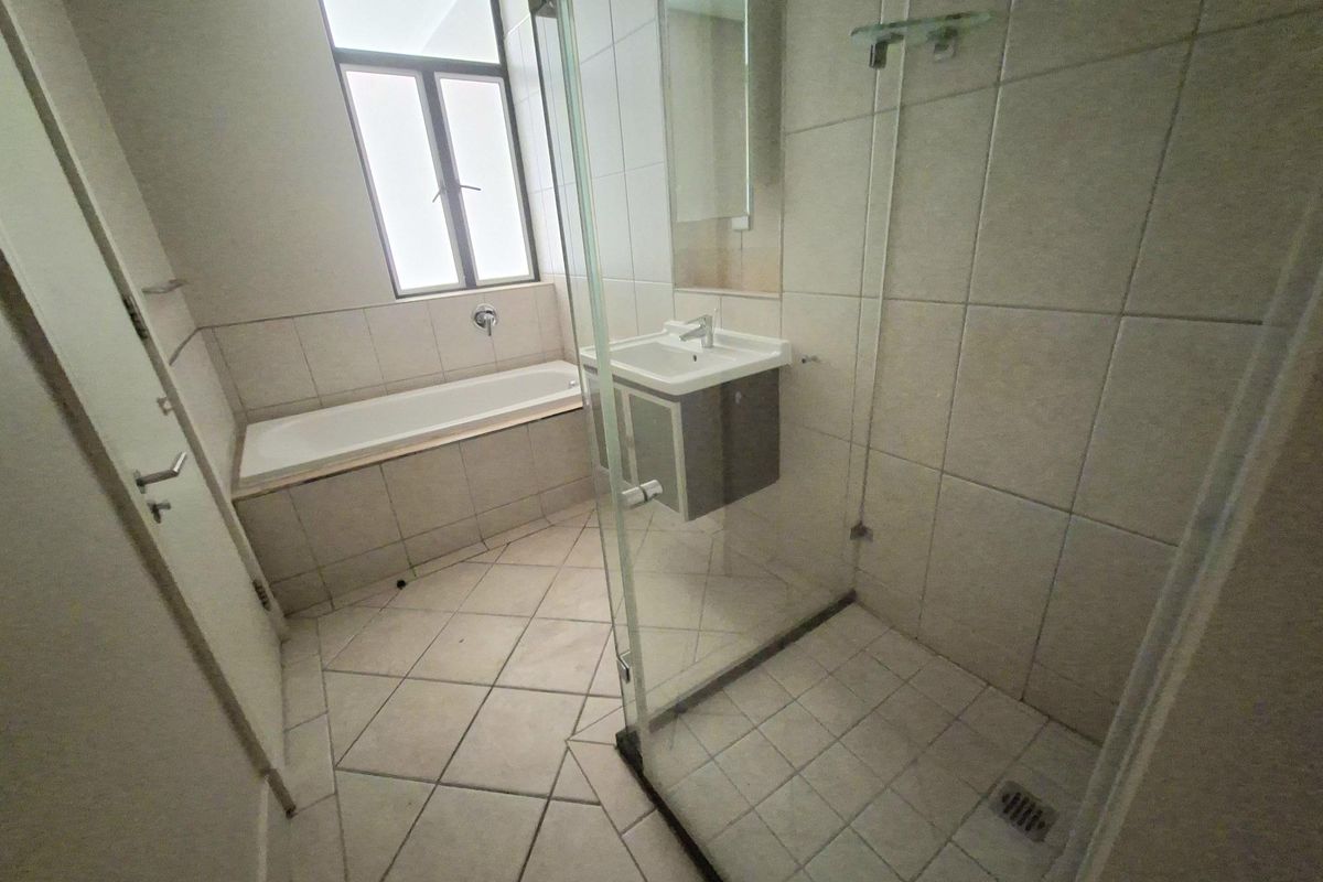 A functional bathroom featuring a built-in bathtub, a separate glass-enclosed shower, and a vanity basin with tiled finishes throughout.