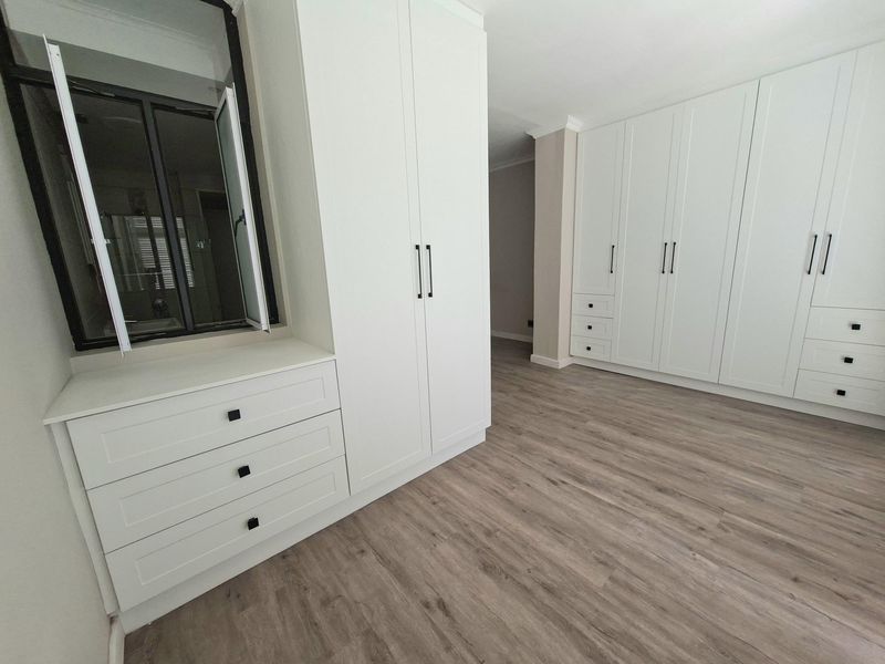 A bright, modern bedroom featuring extensive white built-in cabinetry and high-quality laminate wood flooring.
