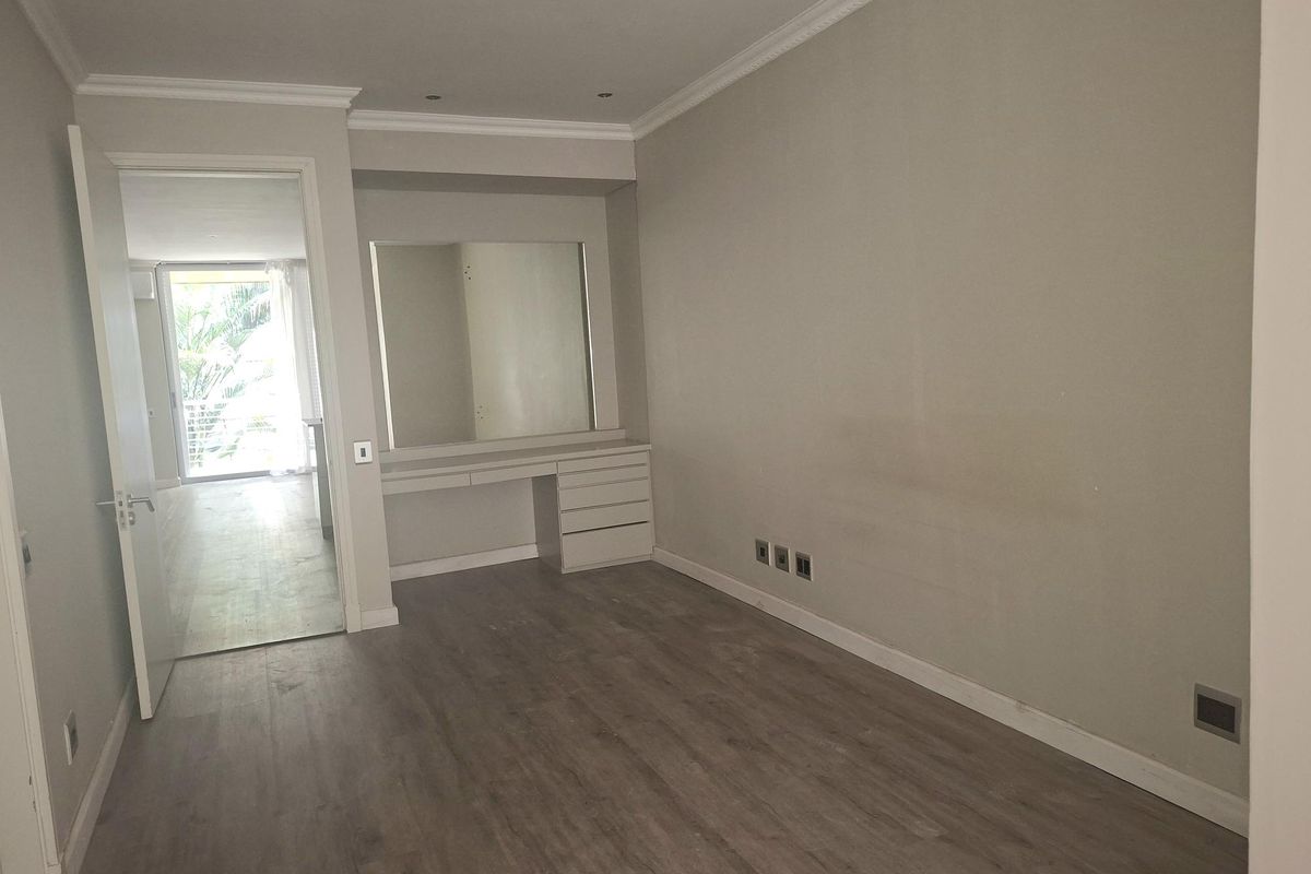 A vacant bedroom featuring laminate flooring, crown molding, and a built-in vanity unit with an integrated mirror.