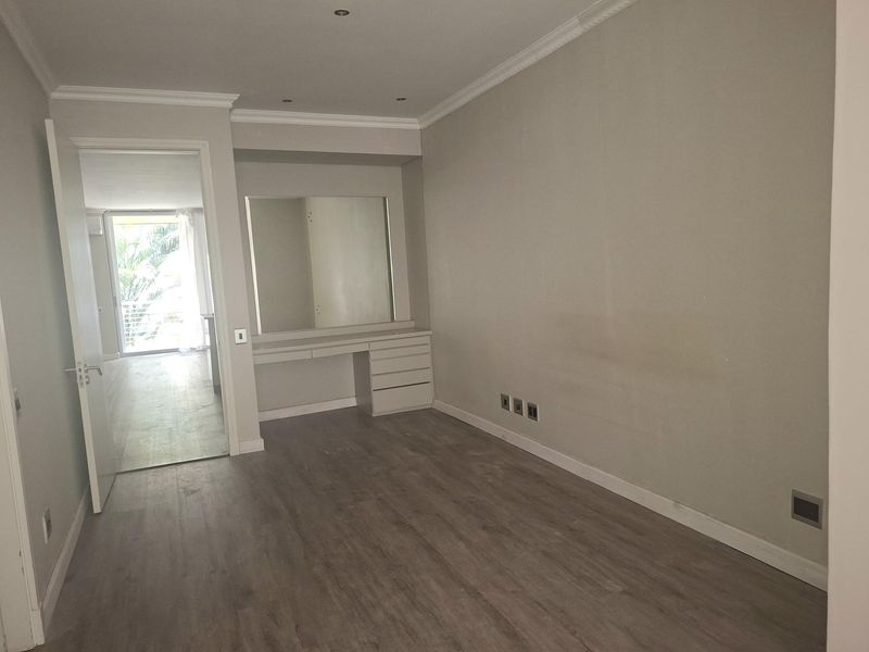 A vacant bedroom featuring laminate flooring, crown molding, and a built-in vanity unit with an integrated mirror.