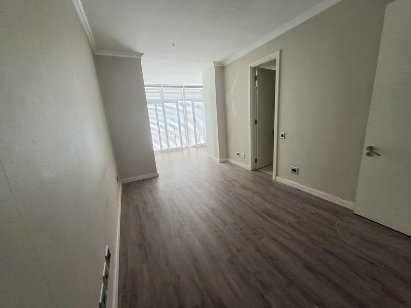 An empty bedroom featuring laminate flooring, neutral walls, and shutter doors leading to an outdoor area.
