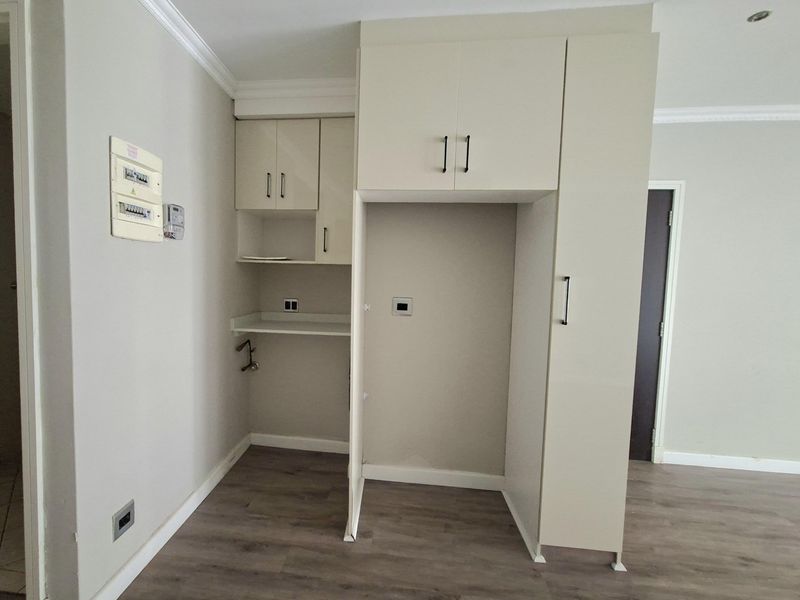 A functional kitchen area featuring built-in cabinetry, laminate flooring, and a dedicated appliance recess, presenting a clean and neutral space ready for customization.