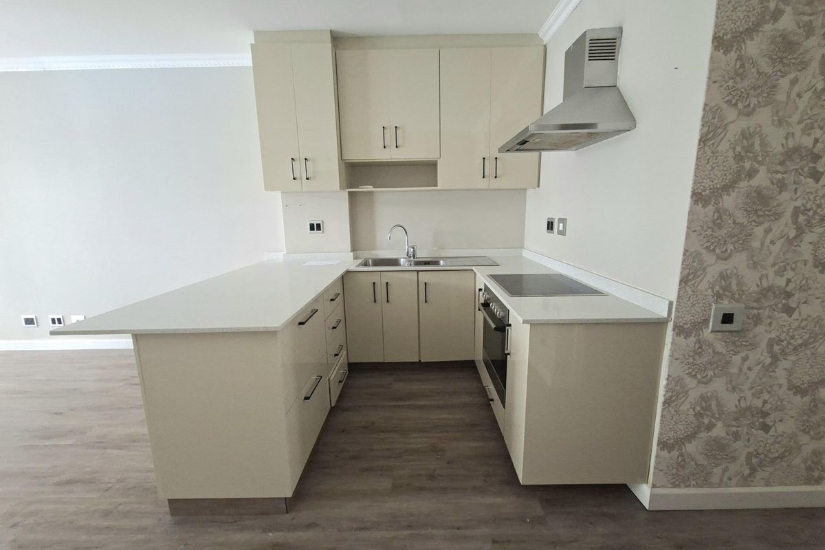 A modern, compact kitchen featuring high-gloss cabinetry, stone countertops, integrated appliances, and durable laminate flooring in an open-plan layout.