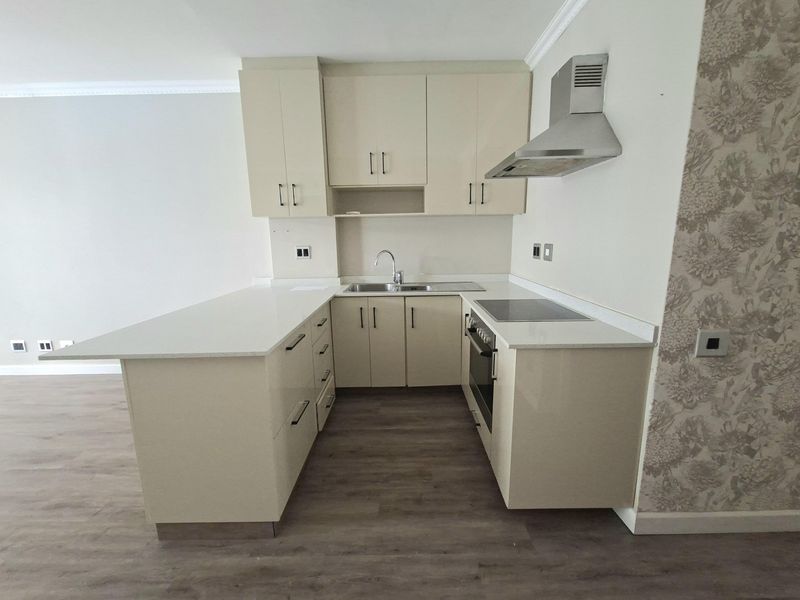 A modern, compact kitchen featuring high-gloss cabinetry, stone countertops, integrated appliances, and durable laminate flooring in an open-plan layout.
