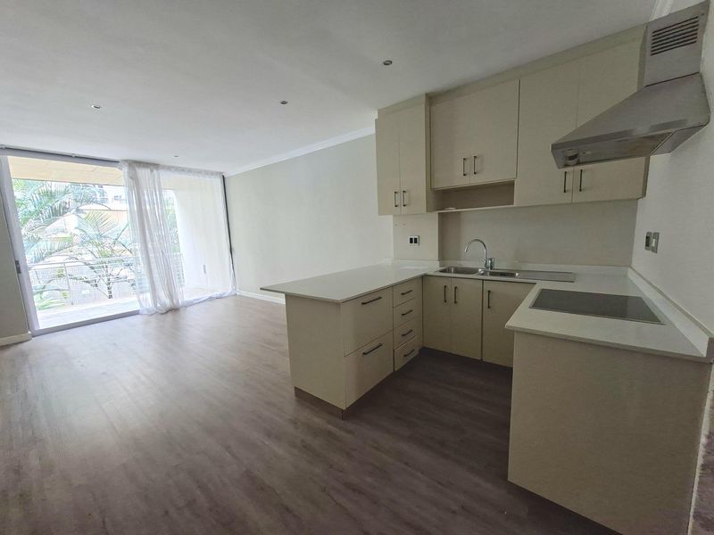 Modern open-plan kitchen and living area featuring neutral cabinetry, integrated appliances, laminate flooring, and direct access to a private balcony.