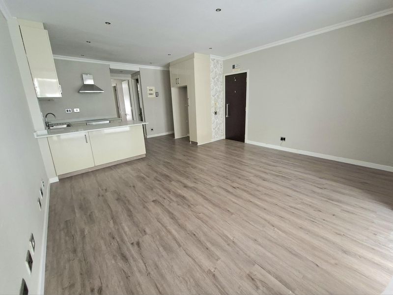Spacious open-plan living area featuring modern laminate flooring, recessed lighting, and a compact, well-maintained kitchen with built-in cabinetry and stainless steel extractor.