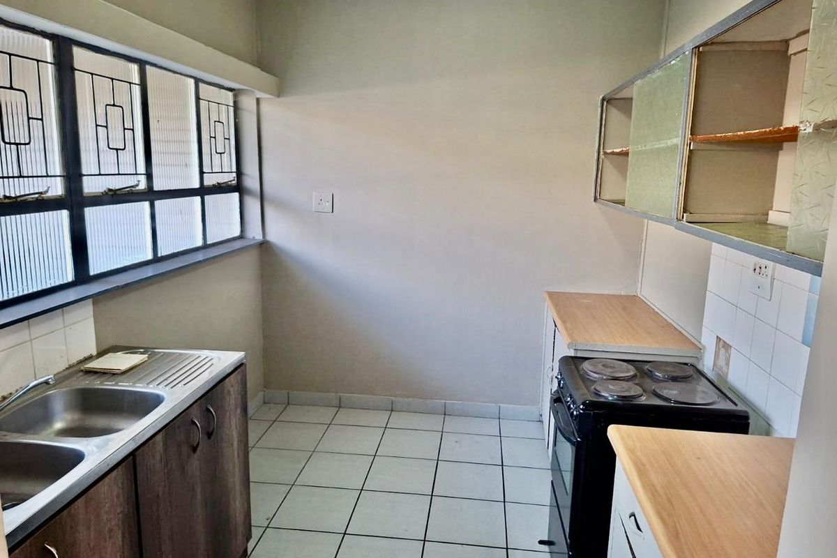 A functional kitchen featuring tiled flooring, double sink, laminate countertops, and an electric stove, requiring cosmetic updates to modernize the space.
