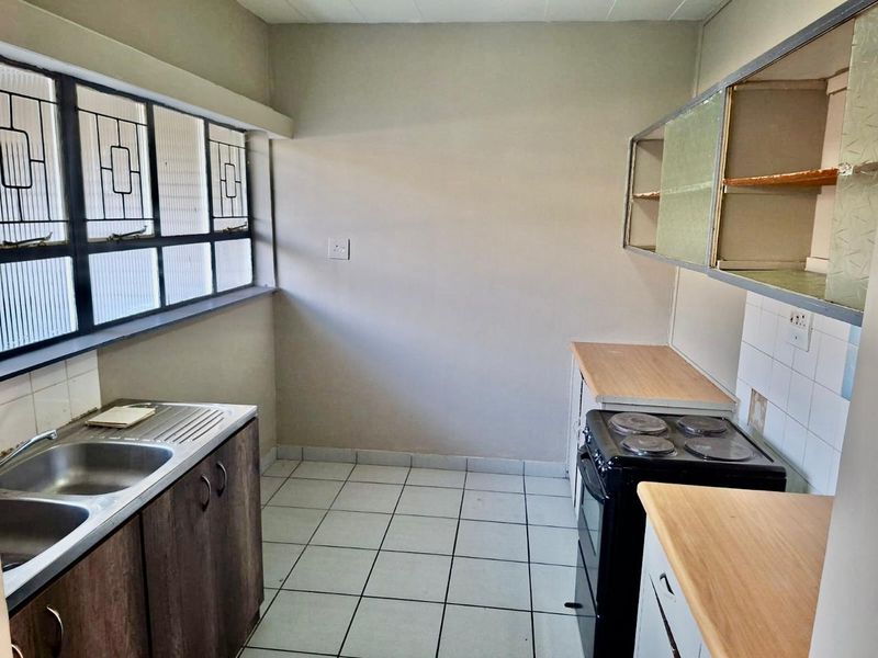 A functional kitchen featuring tiled flooring, double sink, laminate countertops, and an electric stove, requiring cosmetic updates to modernize the space.