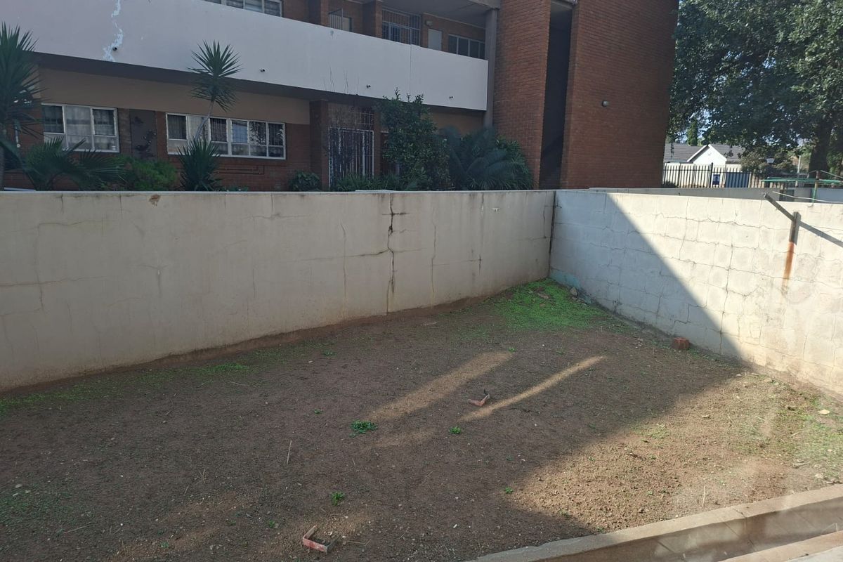A rear courtyard area featuring a boundary wall and concrete apron, currently consisting of bare soil and in need of landscaping.
