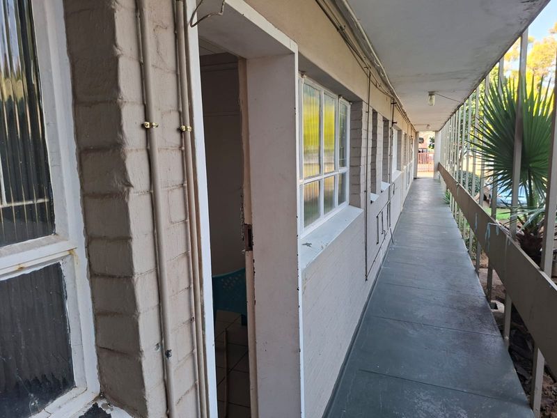 An exterior apartment walkway featuring painted brick walls, exposed electrical conduit, and a metal balustrade overlooking the grounds.