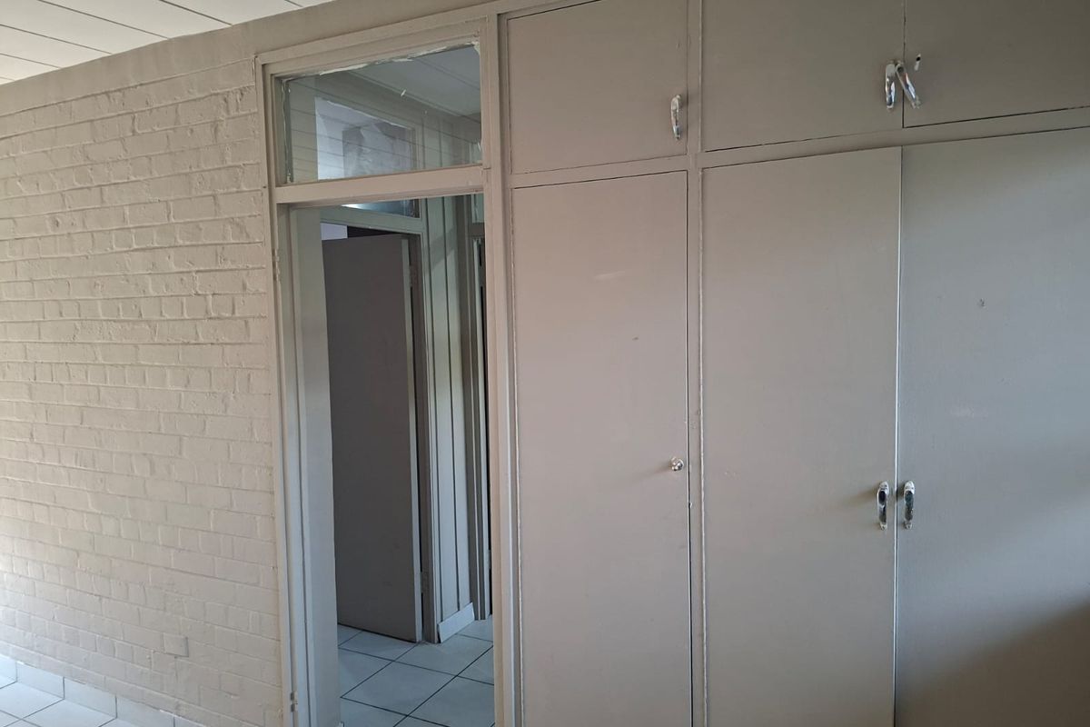 Bedroom featuring built-in cupboards, tiled flooring, and a painted brick wall, offering a blank canvas for renovation or interior design updates.